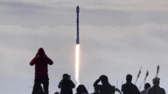 In this view from Playalinda Beach at Canaveral National Seashore, visitors watch a Falcon 9 SpaceX rocket with a payload of approximately 60 satellites for SpaceX's Starlink broadband network lift off from Space Launch Complex 40 at the Cape Canaveral Air Force Station in Cape Canaveral, Fla., Wednesday, Jan. 29, 2020.  (Joe Burbank/Orlando Sentinel via AP)