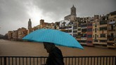 Seorang pria memegang payung saat melintasi jembatan di atas sungai Onyar ketika ada badai di Girona, Spanyol, Kamis (23/1) (AP Photo / Emilio Morenatti)