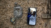 Seorang tukang cukur pinggir jalan tengah memotong rambut yang terpantul di sebuah cermin di samping gambar dewa Hindu di Kolkata, India, Sabtu, (25/1). (AP Photo / Bikas Das)
