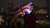 Bendera Inggris berkibar di belakang para warga yang menari di depan Kompleks Parlemen pada Jumat (31/1), beberapa jam setelah negara mereka resmi hengkang dari Uni Eropa. (AP Photo/Alberto Pezzali)