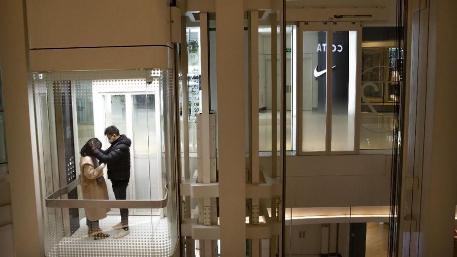Sepasang pasangan terlihat menggenakan masker sambil menaiki lift di pusat perbelanjaan yang hampir kosong di Beijing. (AP Photo/Mark Schiefelbein, File)