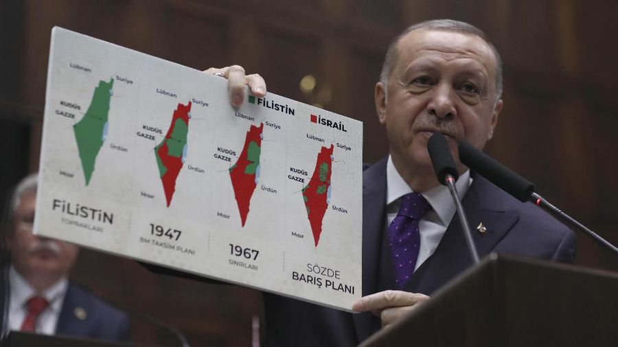 Turkey's President Recep Tayyip Erdogan holds up a placard with what he says is a series of maps of historical Palestine, the 1947 United Nations partition plan on Palestine, the 1948-1967 borders between the Palestinian territories and Israel, and a current map of the Palestinian territories without Israeli-annexed areas and settlements, during a speech at the parliament, in Ankara, Turkey, Wednesday, Feb. 5, 2020. Erdogan denounced U.S. President Donald Trump's recent Middle East peace plan.(AP Photo/Burhan Ozbilici)