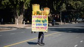 Penjual makanan ringan menyeimbangkan ‘kedai’ di kepalanya ketika melintasi sebuah jalan di dekat India Gate di New Delhi, Kamis (13/2). (Photo by Sajjad HUSSAIN / AFP)