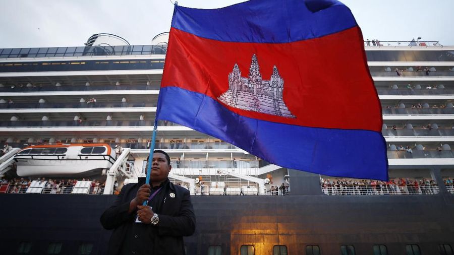 Passengers react after they disembarked from the MS Westerdam, back, at the port of Sihanoukville, Cambodia, Friday, Feb. 14, 2020. Hundreds of cruise ship passengers long stranded at sea by virus fears cheered as they finally disembarked Friday and were welcomed to Cambodia. (AP Photo/Heng Sinith)