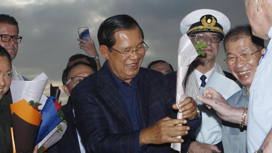 Passengers react after they disembarked from the MS Westerdam, back, at the port of Sihanoukville, Cambodia, Friday, Feb. 14, 2020. Hundreds of cruise ship passengers long stranded at sea by virus fears cheered as they finally disembarked Friday and were welcomed to Cambodia. (AP Photo/Heng Sinith)