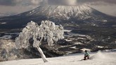 Seorang pria menggunakan papan salju menuruni lembah di hadapan Gunung Yotei di Niseko, Hokkaido, Jepang. Seorang peski yang berkunjung dari Hong Kong, Nguyen Nguyen, mengatakan saat ini jumlah salju kian sedikit. (AP Photo/Jae C. Hong)