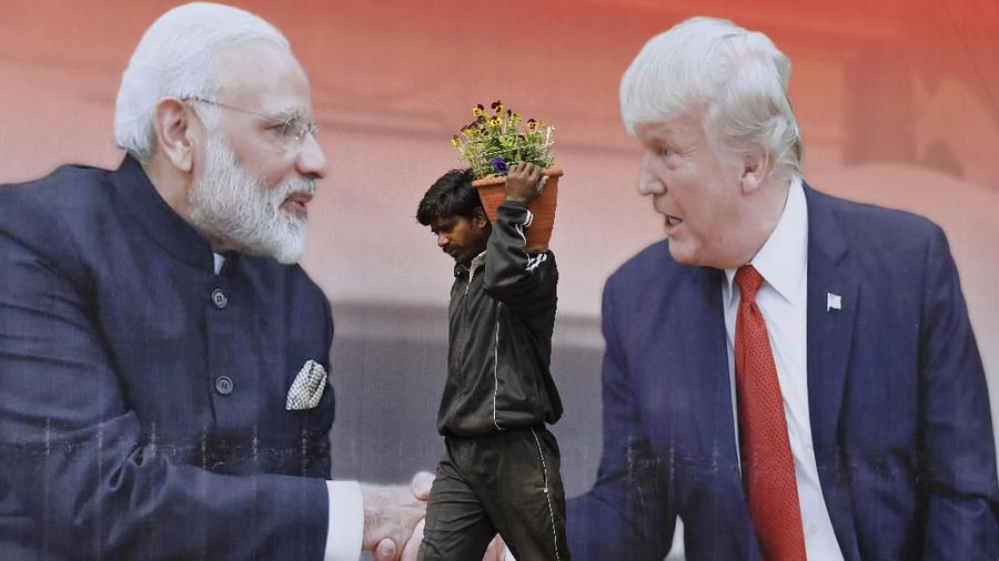 An Indian worker walks carrying flowers to plant passes a billboard featuring U.S. President Donald Trump and Indian Prime Minister Narendra Modi, in Agra, India, Sunday, Feb. 23, 2020. Trump on Monday is expected to travel to Agra to visit the 17th century monument to love, the Taj Mahal. (AP Photo/Rajesh Kumar Singh)