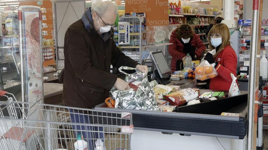Clients and a cashier wear sanitary masks in a supermarket in Casalpusterlengo, Italy, Sunday, Feb. 23, 2020. A dozen Italian towns saw daily life disrupted after the deaths of two people infected with the virus from China and a pair of case clusters without direct links to the outbreak abroad. A rapid spike in infections prompted authorities in the northern Lombardy and Veneto regions to close schools, businesses and restaurants and to cancel sporting events and Masses. (AP Photo/Luca Bruno)