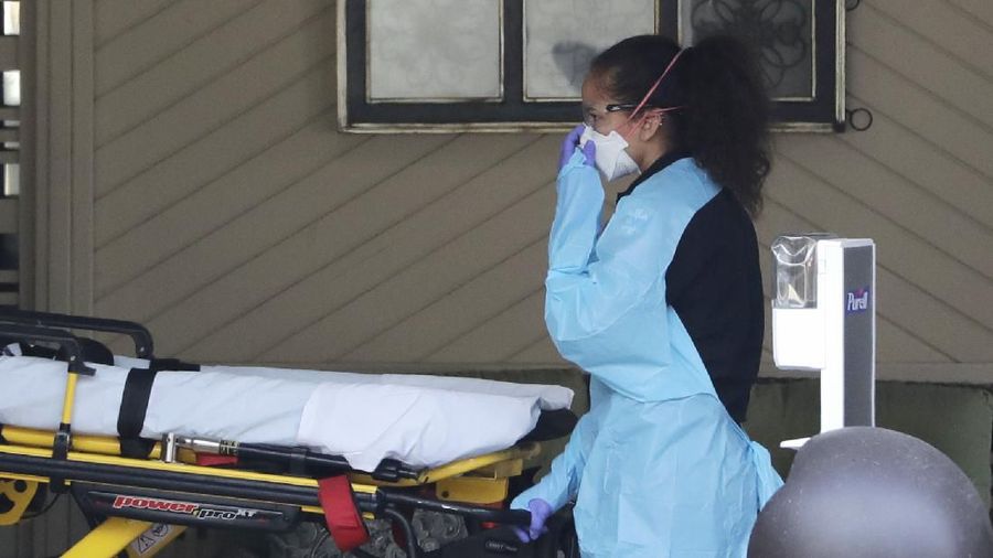A staff member blocks the view as a person is taken by a stretcher to a waiting ambulance from a nursing facility where more than 50 people are sick and being tested for the COVID-19 virus, Saturday, Feb. 29, 2020, in Kirkland, Wash. Health officials reported two cases of COVID-19 virus connected to the Life Care Center of Kirkland. One is a Life Care worker, a woman in her 40s who is in satisfactory condition at a hospital, and the other is a woman in her 70s and a resident at Life Care who is hospitalized in serious condition. Neither have traveled out of the country. (AP Photo/Elaine Thompson)