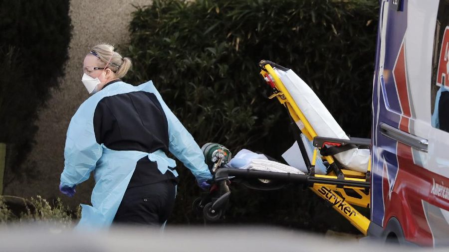 A staff member blocks the view as a person is taken by a stretcher to a waiting ambulance from a nursing facility where more than 50 people are sick and being tested for the COVID-19 virus, Saturday, Feb. 29, 2020, in Kirkland, Wash. Health officials reported two cases of COVID-19 virus connected to the Life Care Center of Kirkland. One is a Life Care worker, a woman in her 40s who is in satisfactory condition at a hospital, and the other is a woman in her 70s and a resident at Life Care who is hospitalized in serious condition. Neither have traveled out of the country. (AP Photo/Elaine Thompson)