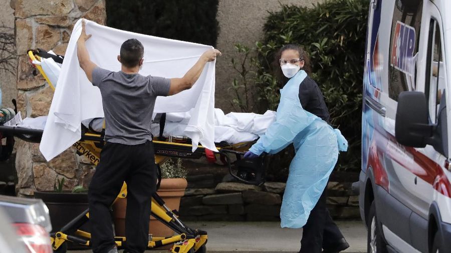 A staff member blocks the view as a person is taken by a stretcher to a waiting ambulance from a nursing facility where more than 50 people are sick and being tested for the COVID-19 virus, Saturday, Feb. 29, 2020, in Kirkland, Wash. Health officials reported two cases of COVID-19 virus connected to the Life Care Center of Kirkland. One is a Life Care worker, a woman in her 40s who is in satisfactory condition at a hospital, and the other is a woman in her 70s and a resident at Life Care who is hospitalized in serious condition. Neither have traveled out of the country. (AP Photo/Elaine Thompson)