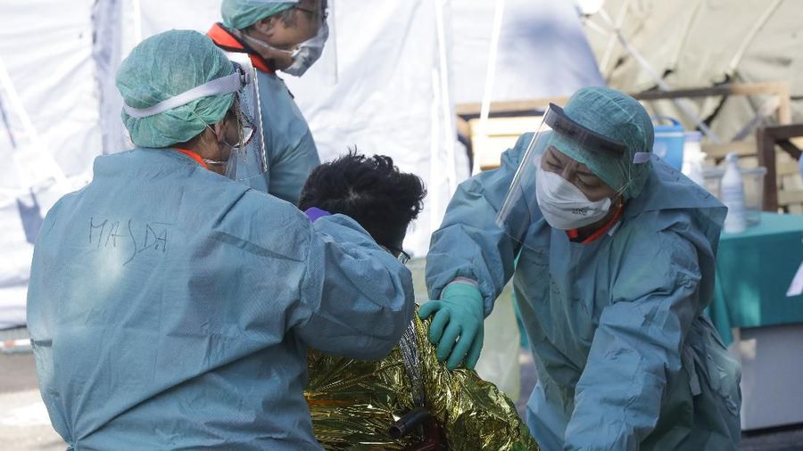 A man wrapped in a survival blanket is assisted by medical staff upon his arrival at one of the emergency structures that were set up to ease procedures at the Brescia hospital, Italy, Monday, March 16, 2020. For most people, the new coronavirus causes only mild or moderate symptoms. For some, it can cause more severe illness, especially in older adults and people with existing health problems. (AP Photo/Luca Bruno)