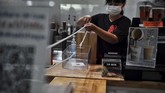 Seorang barista atau peracik kopi di kafe Art of Coffee menggunakan sistem katrol untuk memberikan uang kembalian pada pelanggan yang membeli kopi. Sistem ini digunakan untuk menjaga jarak dan mencegah penyebaran virus corona yang menyebabkan COVID 19. (Lillian SUWANRUMPHA / AFP)
