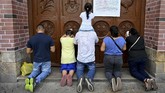 Di Kolombia, orang-orang memanjatkan doa di depan pintu gereja Basilica Yang Maha Penyembuh, berharap wabah corona segera mereda. (Luis ROBAYO / AFP)