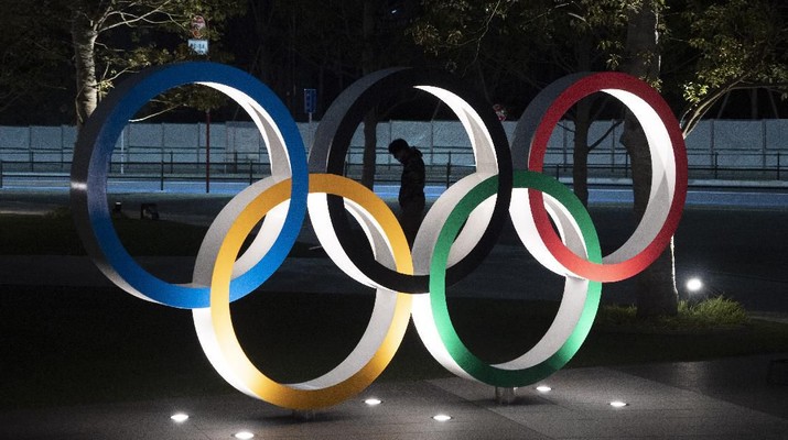A man is seen through the Olympic rings in front of the New National Stadium in Tokyo, Tuesday, March 24, 2020. IOC President Thomas Bach has agreed 