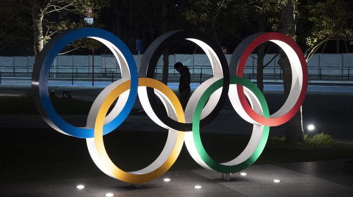 Olimpiade Tokyo (AP Photo/Jae C. Hong) A man is seen through the Olympic rings in front of the New National Stadium in Tokyo, Tuesday, March 24, 2020. IOC President Thomas Bach has agreed