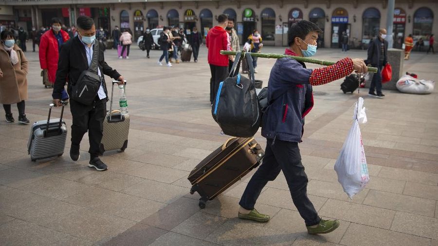 A traveler wearing a face mask carries his luggage at the Beijing Railway Station in Beijing, Wednesday, March 25, 2020. Some train stations and bus services reopened in China's Hubei Province on Wednesday and people who passed a health check would finally be allowed to travel for the first time since the coronavirus outbreak surged in January. (AP Photo/Mark Schiefelbein)