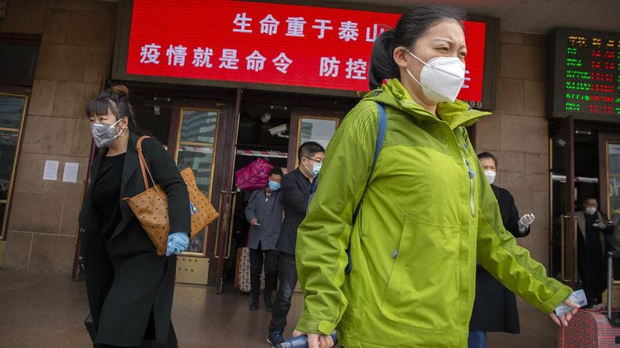 Travelers wearing face masks pull their luggage as they arrive at the Beijing Railway Station in Beijing, Wednesday, March 25, 2020. Some train stations and bus services reopened in China's Hubei Province on Wednesday and people who passed a health check would finally be allowed to travel for the first time since the coronavirus outbreak surged in January. The new coronavirus causes mild or moderate symptoms for most people, but for some, especially older adults and people with existing health problems, it can cause more severe illness or death. The sign reads 