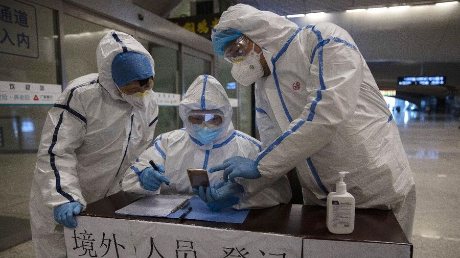 Health workers check details of a passenger arriving from Beijing at the train station in Wuhan in central China's Hubei province on Sunday, March 29, 2020. Wuhan, the city at the center of China's virus outbreak, has reopened subways and long-distance train service in another step toward ending restrictions that confined millions of people to their homes. Chinese characters read 