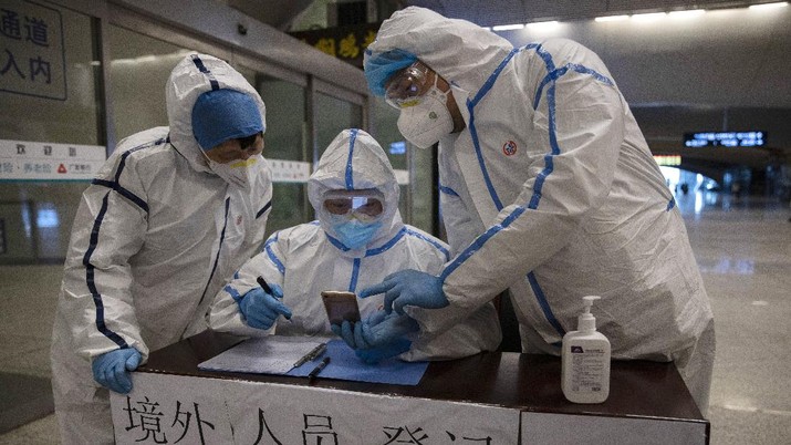 Health workers check details of a passenger arriving from Beijing at the train station in Wuhan in central China's Hubei province on Sunday, March 29, 2020. Wuhan, the city at the center of China's virus outbreak, has reopened subways and long-distance train service in another step toward ending restrictions that confined millions of people to their homes. Chinese characters read 