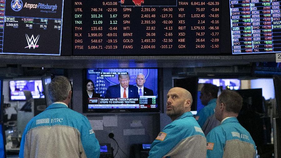 FILE - In this March 18, 2020, file photo traders at the New York Stock Exchange watch President Donald Trump's televised White House news conference in New York. When President Donald Trump speaks, financial markets gyrate and quiver in real time. (AP Photo/Mark Lennihan, File)
