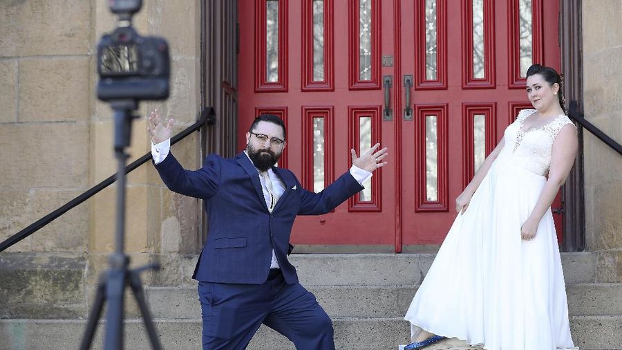 With a camera mounted on a tripod, newlyweds Andrew and Emilye West, of Madison, walk around Capitol Square using the self-timer to take pictures on their wedding day, in Madison, Wis., Saturday, April 4, 2020. The couple planned their April 4 wedding last fall, which included family and friends, but had to change plans since the spread of COVID-19. They got married at a park in the town of Burke surrounded by a small group of friends who were practicing social distancing. (Amber Arnold/Wisconsin State Journal via AP)