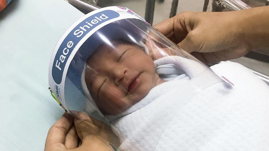 In this Friday, April 3, 2020, photo released by Paolo Hospital Samutprakarn, a nurse adjusts tiny face shield for a newborn baby to protect from new coronavirus at the newborn nursery of the hospital in Samutprakarn province, central Thailand. The new coronavirus causes mild or moderate symptoms for most people, but for some, especially older adults and people with existing health problems, it can cause more severe illness or death. (Paolo Hospital Samutprakarn via AP)