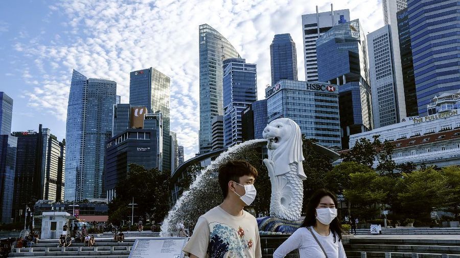 In this March 14, 2020, photo, a couple wearing face masks walk past the Merlion statue in Singapore. As the virus outbreak spreads ever further, it's becoming clear that some strategies are more likely to succeed in containing it: pro-active efforts to track down and isolate cases, access to basic, affordable public health and clear, reassuring messaging from leaders. (AP Photo/Ee Ming Toh)