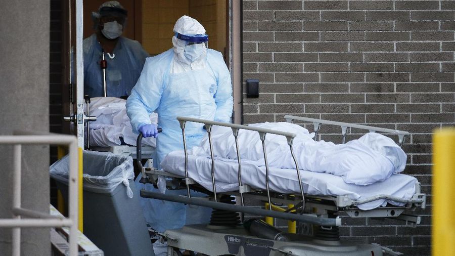 Medical workers wearing personal protective equipment wheel bodies to a refrigerated trailer serving as a makeshift morgue at Wyckoff Heights Medical Center, Monday, April 6, 2020, in New York. The new coronavirus causes mild or moderate symptoms for most people, but for some, especially older adults and people with existing health problems, it can cause more severe illness or death. (AP Photo/John Minchillo)