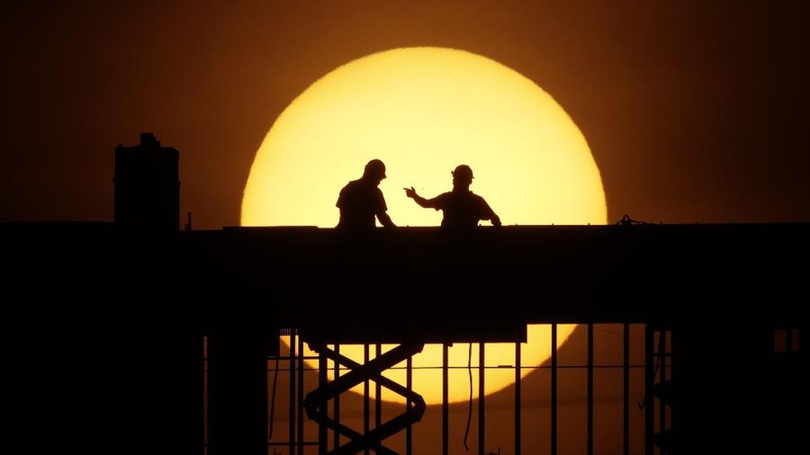 Workers are silhouetted against the rising sun as they toil on a new apartment building in Kansas City, Mo. Wednesday, April 8, 2020. Construction workers are among the people exempt from the city's stay-at-home order which remains in effect in an effort to slow the spread of the new coronavirus. (AP Photo/Charlie Riedel)