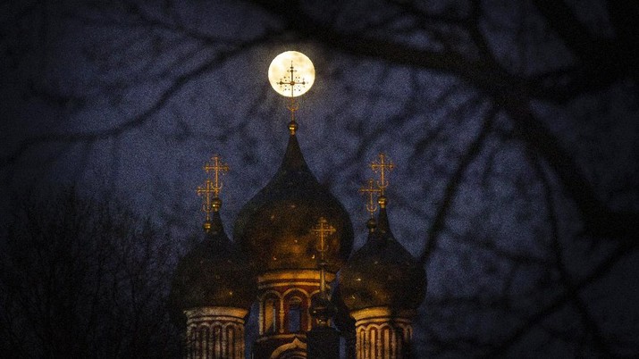 The Supermoon rise behind an illuminated cross from a Christian Orthodox church in Moscow, Russia, Tuesday, April 7, 2020. The phenomenon of 