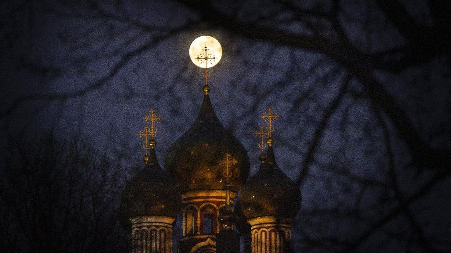 The Supermoon rise behind an illuminated cross from a Christian Orthodox church in Moscow, Russia, Tuesday, April 7, 2020. The phenomenon of