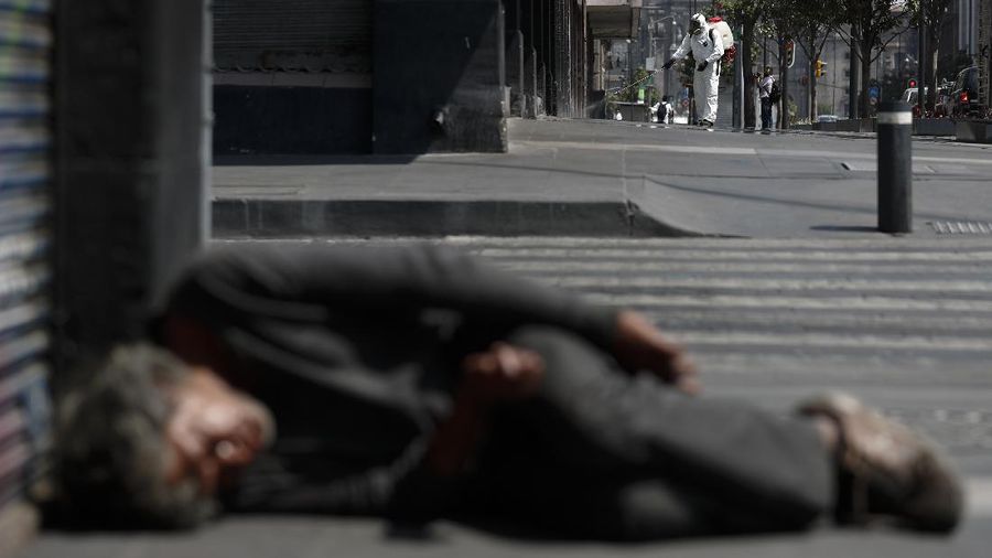 A city worker sprays disinfectant as a man sleeps on the street, in central Mexico City, Monday, April 6, 2020. Mexican President Andres Manuel Lopez Obrador said Sunday there will be no huge economic stimulus program as the country faces the threat of coronavirus-induced crisis almost certainly unlike any it has seen in the past century. (AP Photo/Rebecca Blackwell)