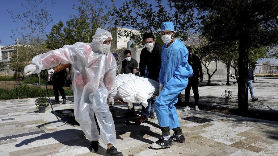 People wearing protective clothing carry the body of a victim who died after being infected with the new coronavirus at a cemetery just outside Tehran, Iran, Monday, March 30, 2020. The new coronavirus causes mild or moderate symptoms for most people, but for some, especially older adults and people with existing health problems, it can cause more severe illness or death. (AP Photo/Ebrahim Noroozi)