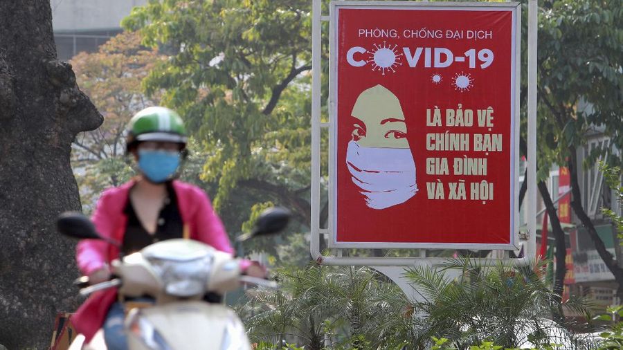 A motorcyclist drives past a poster calling people to take care of their health against the new coronavirus in Hanoi, Vietnam Tuesday, April 14, 2020. The new coronavirus causes mild or moderate symptoms for most people, but for some, especially older adults and people with existing health problems, it can cause more severe illness or death. (AP Photo/Hau Dinh)