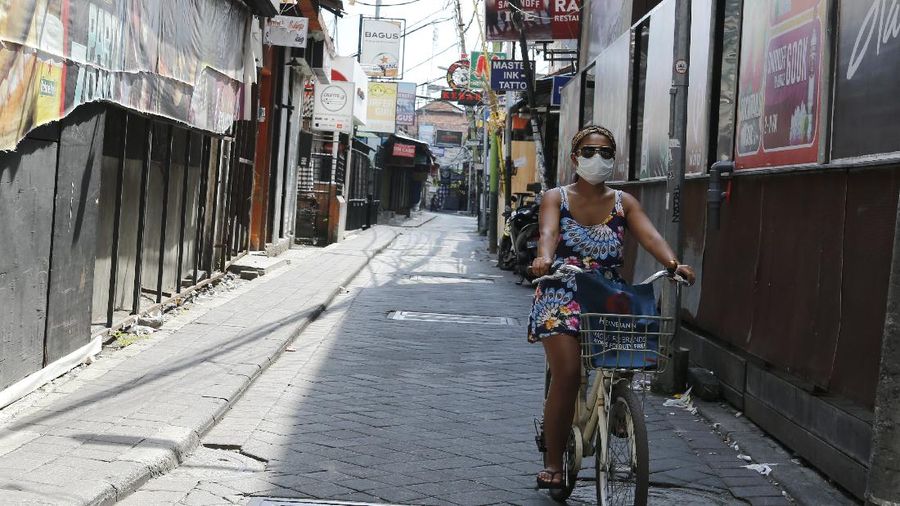 A woman wears a face mask to help stop the spread of the coronavirus as she bicycles down an empty road in Bali, Indonesia, Tuesday, April 14, 2020. Forced apart by the coronavirus pandemic, Southeast Asian leaders linked up by video Tuesday to plot a strategy to overcome a crisis that has threatened their economies and bound millions of people in their homes under lockdowns. (AP Photo/Firdia Lisnawati)