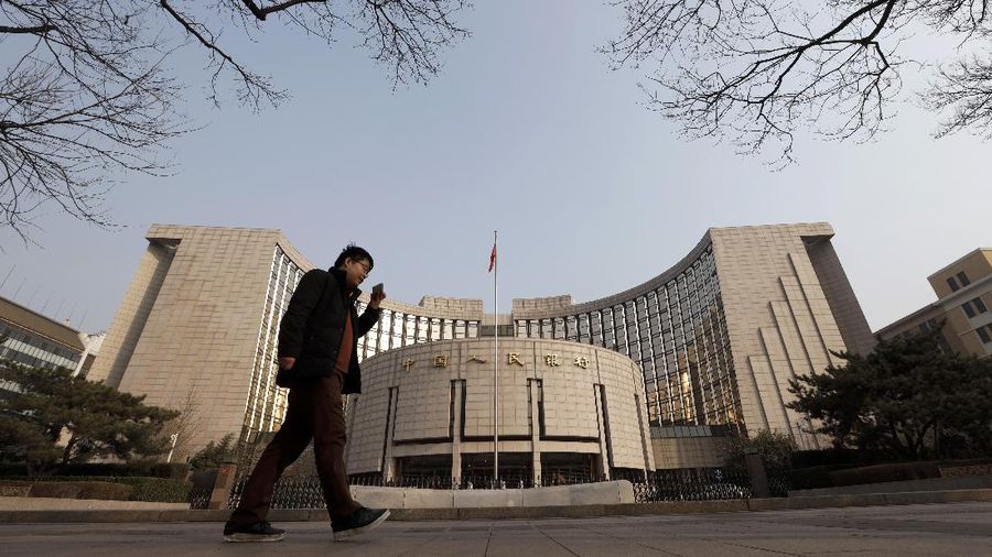 A man walks past China's central bank, or the People's Bank of China, in Beijing, Sunday, March 10, 2019. China's central bank governor Yi Gang says American and Chinese envoys discussed sticking to promises to avoid currency devaluations to boost exports during negotiations aimed at ending a tariff war. (AP Photo/Andy Wong)