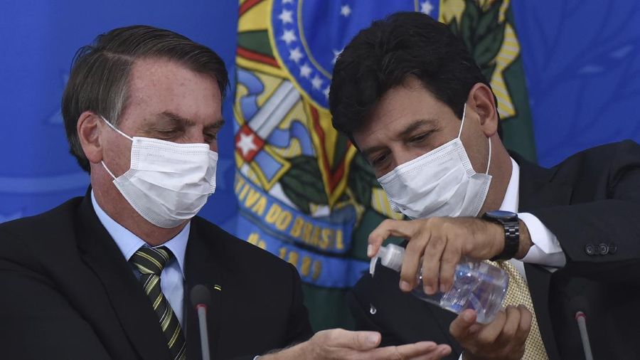 FILE - In this March 18, 2019 file photo, Brazil's Health Minister Luiz Henrique Mandetta, right, gives anti-bacterial gel to President Jair Bolsonaro as they give a press conference on the new coronavirus at Planalto presidential palace in Brasilia, Brazil. Mandetta criticized Bolsonaro’s dismissive handling of the COVID-19 pandemic on national television Sunday night, April 12, and the president’s repeated threats to fire him are worrying health experts who say that amid governmental chaos, the health minister's advice to limit contact and take the virus seriously has played a major role in preventing Brazil’s epidemic from being even worse. (AP Photo/Andre Borges, File )