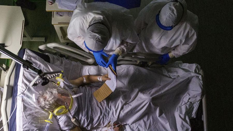 Doctor Giovanni Passeri, top left, with his assistant doctor Mariaconcetta Terracina, has 82-year-old patient Mario read his note about his medical conditions during a routine examination as part of a night shift in his ward in the COVID-19 section of the Maggiore Hospital in Parma, northern Italy Wednesday, April 8, 2020. Mario has been under oxygen CPAP (continuous positive air pressure) headgear ventilation and he could only communicate in writing because the hissing sound of the oxygen made it difficult for him to hear the doctor's voice. Mario's health conditions have been worsening since after his admission on March 28. He died in the evening of April 14. (AP Photo/Domenico Stinellis)