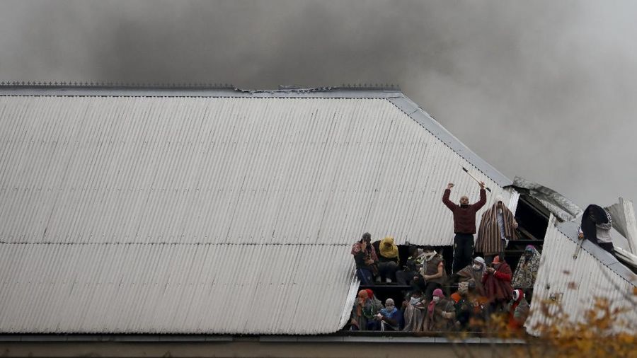 Rioting inmates stand on the roof of the Villa Devoto prison as they protest against authorities who they say are not doing enough to prevent the spread of the new coronavirus, in Buenos Aires, Argentina, Friday, April 24, 2020. (AP Photo/Natacha Pisarenko)