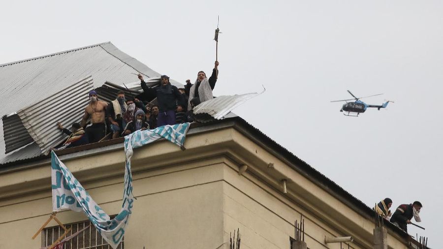 Rioting inmates stand on the roof of the Villa Devoto prison as they protest against authorities who they say are not doing enough to prevent the spread of the new coronavirus, in Buenos Aires, Argentina, Friday, April 24, 2020. (AP Photo/Natacha Pisarenko)