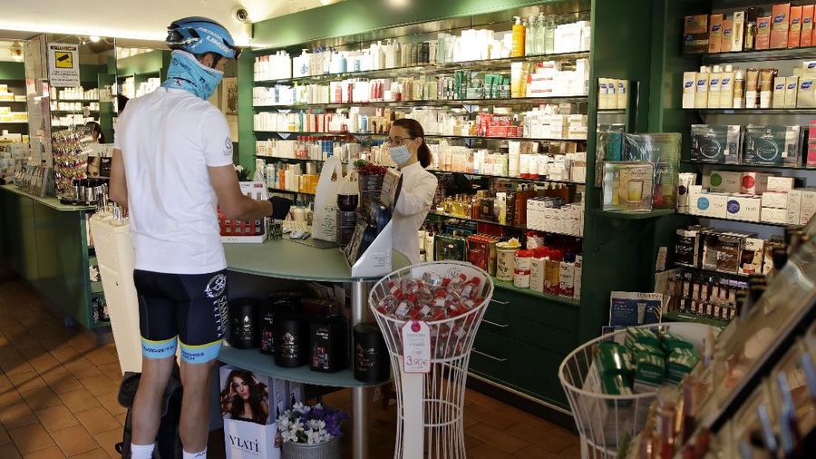 In this image taken on Tuesday, April 14, 2020, Italian professional cyclist Davide Martinelli, collects medicine at a pharmacy to be delivered to residents in Rovato, near Brescia, Northern Italy. There are no fans lining the road. No teammates providing support. And no race to win. Professional cyclist Davide Martinelli has achieved a moral victory, though, by using his bike to help deliver medicine to elderly residents of his hometown in northern Italy during the coronavirus pandemic. (AP Photo/Luca Bruno)