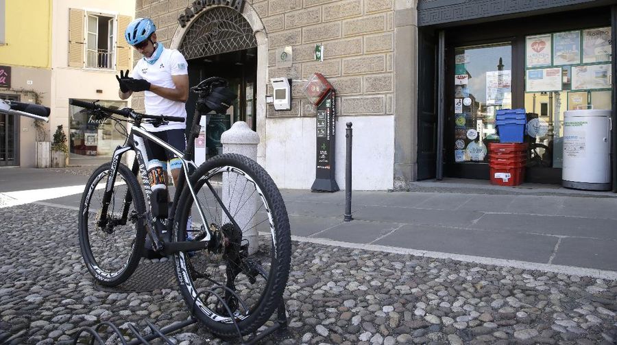 In this image taken on Tuesday, April 14, 2020, Italian professional cyclist Davide Martinelli, collects medicine at a pharmacy to be delivered to residents in Rovato, near Brescia, Northern Italy. There are no fans lining the road. No teammates providing support. And no race to win. Professional cyclist Davide Martinelli has achieved a moral victory, though, by using his bike to help deliver medicine to elderly residents of his hometown in northern Italy during the coronavirus pandemic. (AP Photo/Luca Bruno)