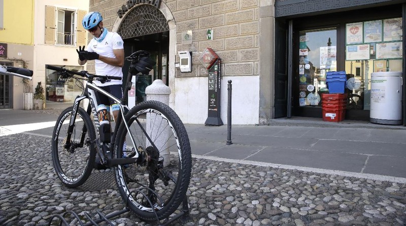 In this image taken on Tuesday, April 14, 2020, Italian professional cyclist Davide Martinelli, collects medicine at a pharmacy to be delivered to residents in Rovato, near Brescia, Northern Italy. There are no fans lining the road. No teammates providing support. And no race to win. Professional cyclist Davide Martinelli has achieved a moral victory, though, by using his bike to help deliver medicine to elderly residents of his hometown in northern Italy during the coronavirus pandemic. (AP Photo/Luca Bruno)