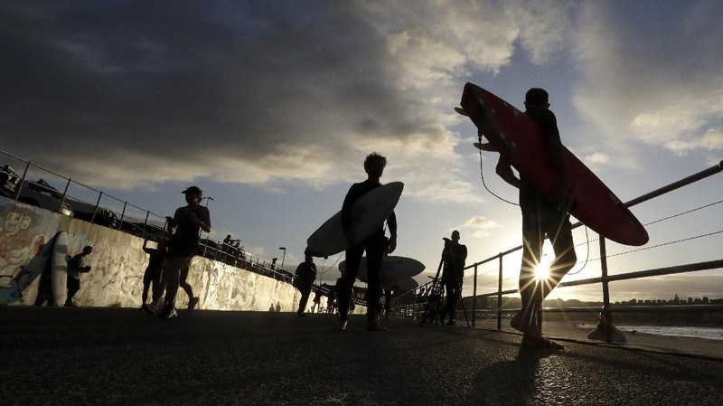 A sign indicates the beach is closed as a surfers arrives for the 7A.M. opening of Bondi Beach in Sydney, Tuesday, April 28, 2020, as coronavirus pandemic restrictions are eased. The beach is open to swimmers and surfers to exercise only. (AP Photo/Rick Rycroft)