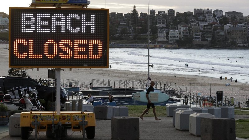 A sign indicates the beach is closed as a surfers arrives for the 7A.M. opening of Bondi Beach in Sydney, Tuesday, April 28, 2020, as coronavirus pandemic restrictions are eased. The beach is open to swimmers and surfers to exercise only. (AP Photo/Rick Rycroft)