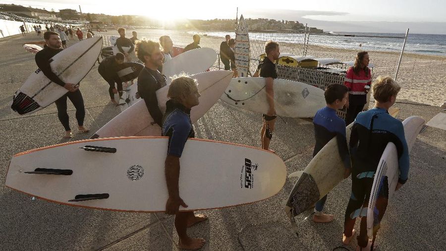 A sign indicates the beach is closed as a surfers arrives for the 7A.M. opening of Bondi Beach in Sydney, Tuesday, April 28, 2020, as coronavirus pandemic restrictions are eased. The beach is open to swimmers and surfers to exercise only. (AP Photo/Rick Rycroft)