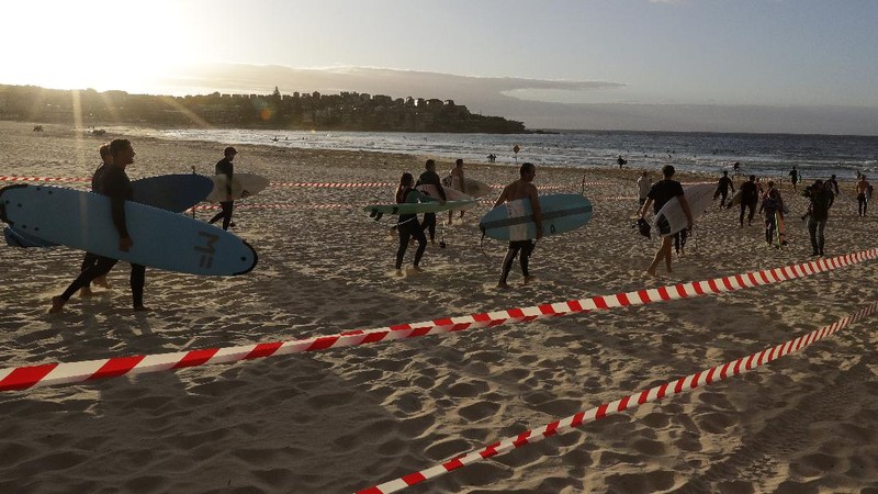 A sign indicates the beach is closed as a surfers arrives for the 7A.M. opening of Bondi Beach in Sydney, Tuesday, April 28, 2020, as coronavirus pandemic restrictions are eased. The beach is open to swimmers and surfers to exercise only. (AP Photo/Rick Rycroft)