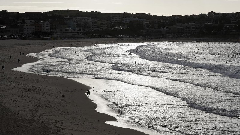 A sign indicates the beach is closed as a surfers arrives for the 7A.M. opening of Bondi Beach in Sydney, Tuesday, April 28, 2020, as coronavirus pandemic restrictions are eased. The beach is open to swimmers and surfers to exercise only. (AP Photo/Rick Rycroft)