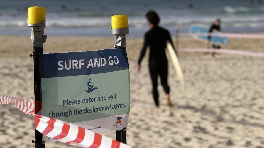 A sign indicates the beach is closed as a surfers arrives for the 7A.M. opening of Bondi Beach in Sydney, Tuesday, April 28, 2020, as coronavirus pandemic restrictions are eased. The beach is open to swimmers and surfers to exercise only. (AP Photo/Rick Rycroft)